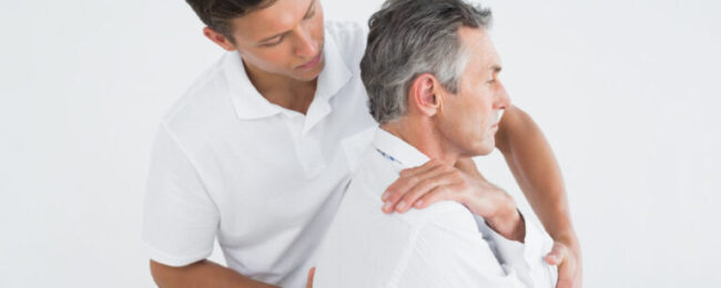 Side view of a male chiropractor examining mature man over white